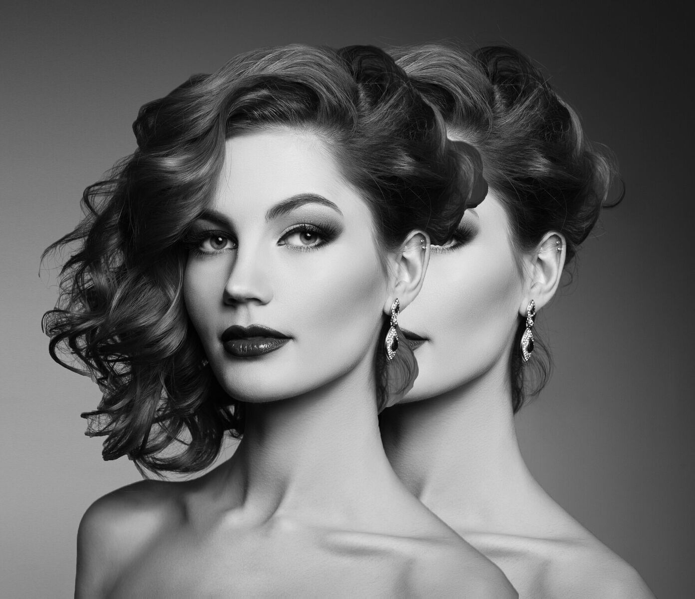 Duplicate image of woman behind herself with makeup on and fancy earrings in black and white
