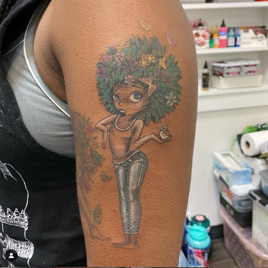 Tattoo of cartoon woman with leaves for an afro and holding a bird in her palm on someone's arm